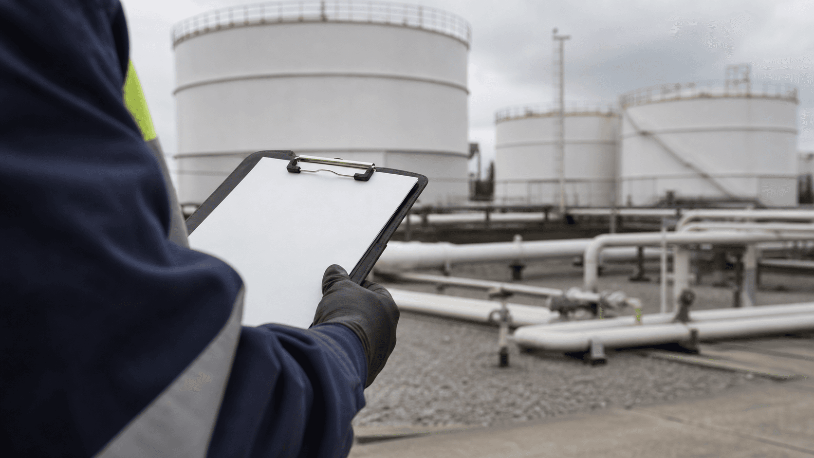An inspector reviewing filled operational paperwork near fuel-storage tanks.